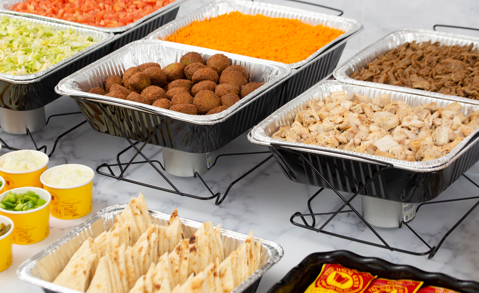 A buffet displays seasoned chicken, flavorful gyro, crispy falafel, fluffy rice, crisp lettuce, ripe tomatoes, and warm pita bread